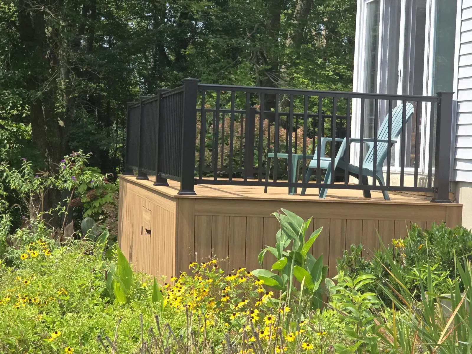 Zenna Decks portfolio: brown deck with dark railing, a light blue chair and flowers around the base